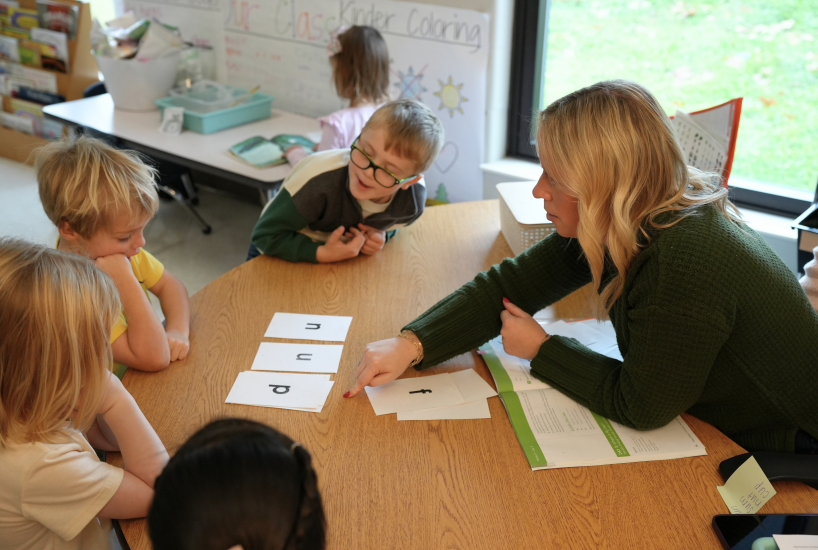 teacher helps a kindergarten sound out a word by pointing at the letters